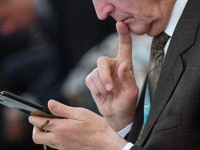 Участник Международного финансового конгресса с мобильным телефоном и очками в руке. Фото: Александр Коряков / Коммерсант
